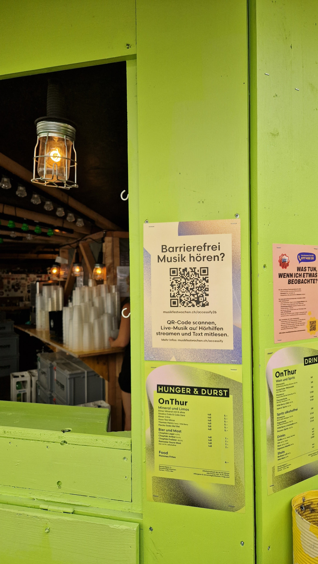 Festivalstand mit dem Plakat «Barrierefrei Musik hören?» und QR-Code zur accessify.live-Webapp